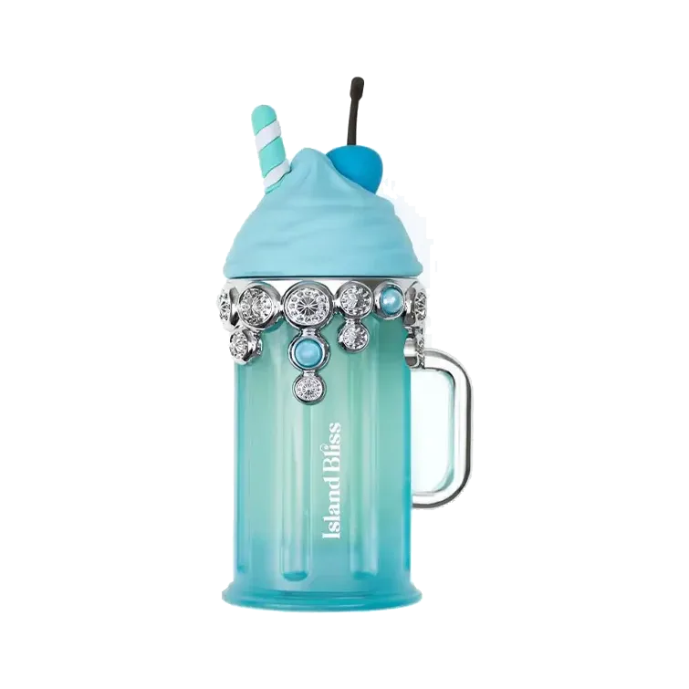 Frasco con forma de vaso de batido en vidrio turquesa, con asa, crema azul esculpida, pajita a rayas y una guirnalda de pedrería alrededor del cuello, sobre fondo blanco.